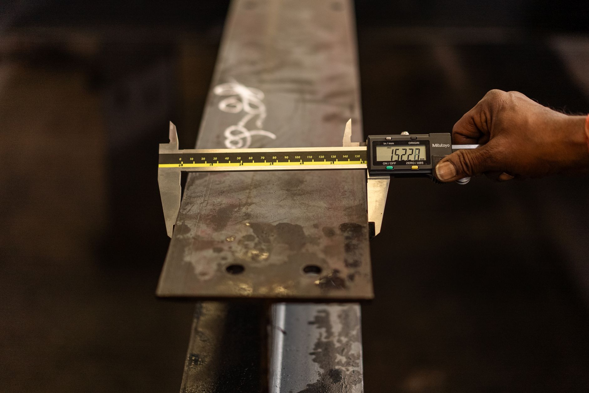 A hand measuring a machined part with a digital caliper